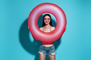 Eğlenme zamanı. Çekici genç Asyalı kadın gülümseyerek ve mavi arka plan karşı dururken kameraya bakıyor