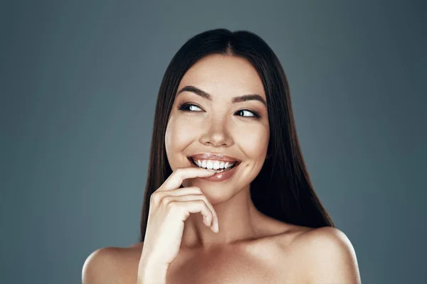 Beautiful perfection. Beautiful young Asian woman looking away and smiling while standing against grey background