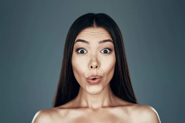 Juguetón. Sorprendido joven mujer asiática mirando a la cámara y sonriendo mientras está de pie sobre fondo gris —  Fotos de Stock