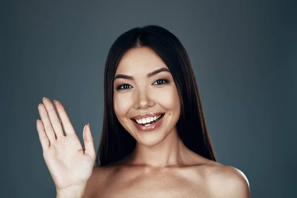 Merhaba! Güzel genç Asyalı kadın kameraya bakıyor ve gri arka planda dururken gülümsüyor — Stok fotoğraf