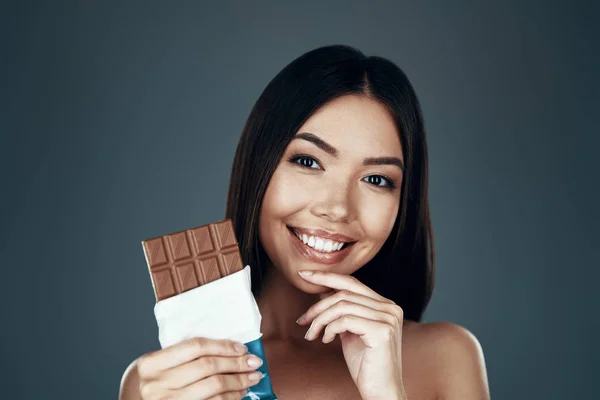 Amante de chocolate. Linda jovem mulher asiática sorrindo e olhando para a câmera enquanto estava de pé contra fundo cinza — Fotografia de Stock
