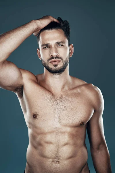 Handsome young shirtless man looking at camera while standing against grey background