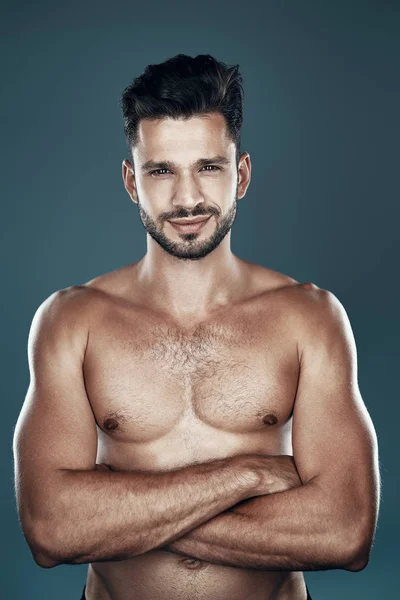 Handsome young shirtless man looking at camera and smiling while standing against grey background