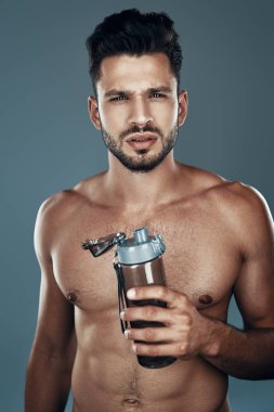 Yakışıklı genç gömleksiz adam gri arka plan karşı dururken kameraya bakıyor