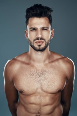 Yakışıklı genç gömleksiz adam gri arka plan karşı dururken kameraya bakıyor