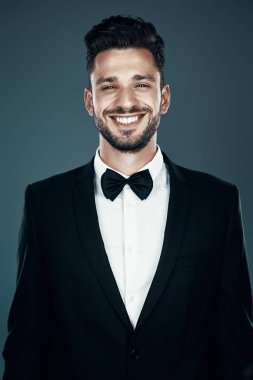 Gri arka plan aleyhine dururken kameraya bakan ve gülümseyen papyonlu büyüleyici genç adam