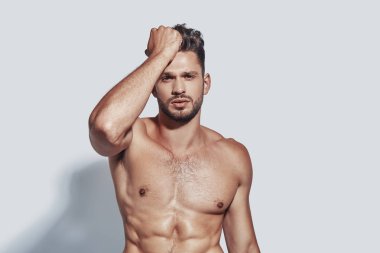 Yakışıklı genç gömleksiz adam gri arka plan karşı dururken kameraya bakıyor