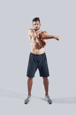 Gri arka plan aleyhine ayakta iken spor giyim ısınma yakışıklı genç adam tam uzunlukta