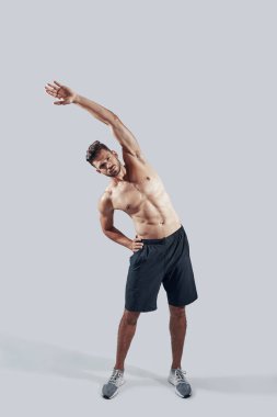 Gri arka plan aleyhine ayakta iken spor giyim ısınma yakışıklı genç adam tam uzunlukta