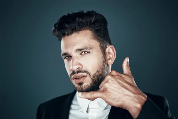 Okouzlující mladý muž ve formální opotřebení ukazuje mi gesto a dívám se na kameru, zatímco stojím proti šedému pozadí — Stock fotografie