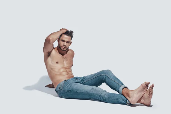 Handsome young shirtless man looking at camera while sitting against grey background — Stock Photo, Image