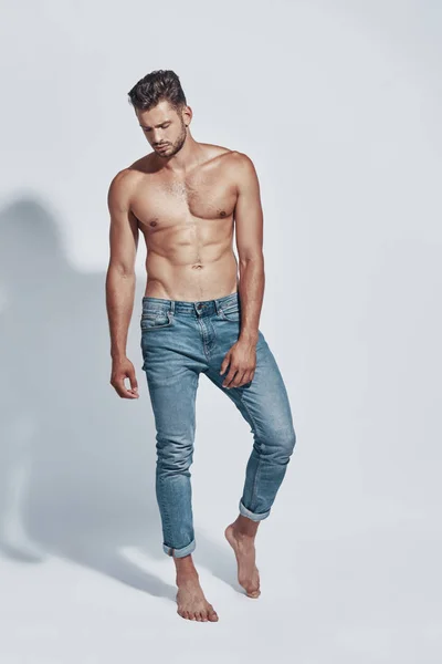 Piena lunghezza di bello giovane uomo senza maglietta in posa mentre in piedi contro sfondo grigio — Foto Stock
