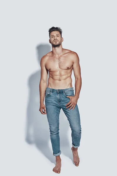Full length of handsome young shirtless man looking at camera while standing against grey background — Stock Photo, Image