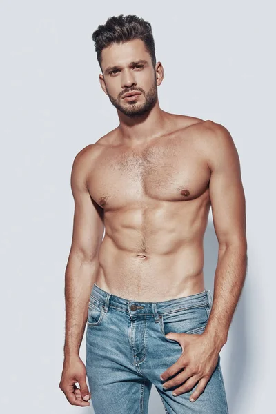 Handsome young shirtless man looking at camera while standing against grey background — Stock Photo, Image