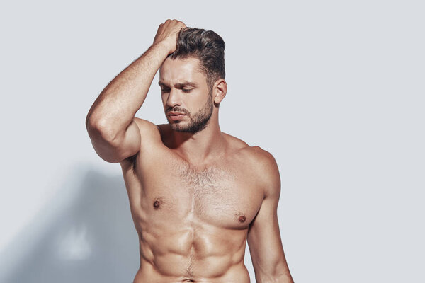 Красивый молодой мужчина без рубашки позирует, стоя на сером фоне
