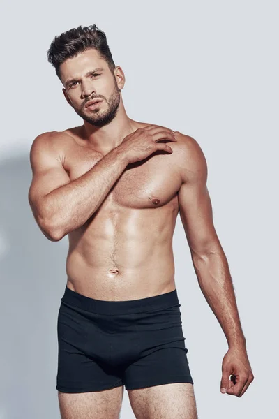 Handsome young shirtless man looking at camera while standing against grey background — Stock Photo, Image