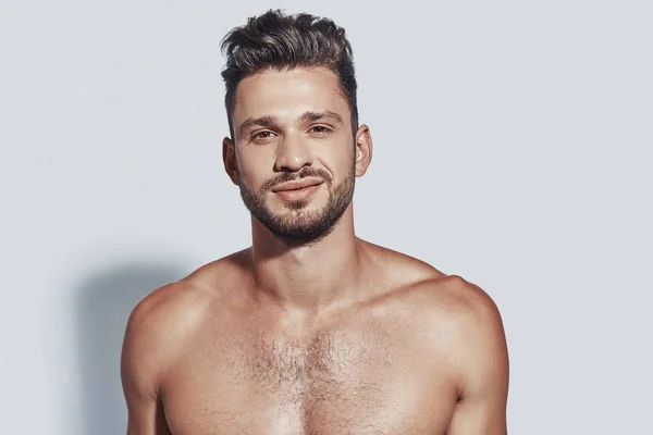 Handsome young shirtless man looking at camera and smiling while standing against grey background — Stock Photo, Image