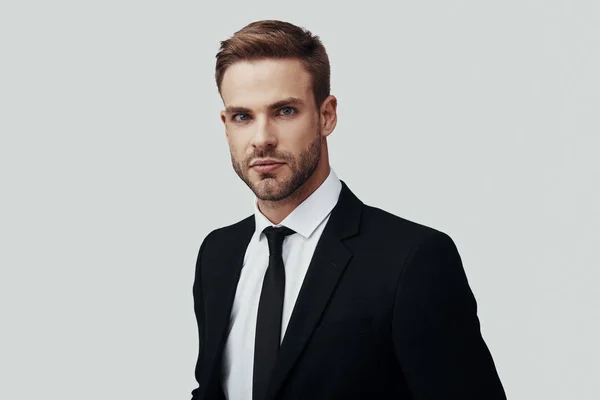 Handsome young man in formalwear looking at camera while standing against grey background — Stock Photo, Image