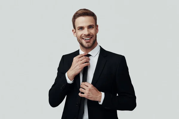 Bello giovane in abbigliamento formale guardando la fotocamera e sorridendo mentre in piedi sullo sfondo grigio — Foto Stock