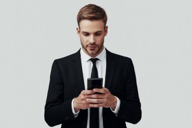 Gri arka plan aleyhine dururken akıllı telefon kullanarak formalwear yakışıklı genç adam
