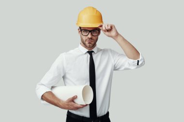 Gri arka planda dururken kameraya bakan kasklı yakışıklı genç adam