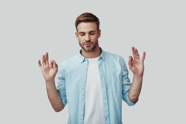 Yakışıklı genç adam meditasyon ve gri arka plan karşı dururken gözleri kapalı tutmak