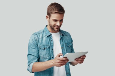 Yakışıklı genç adam gülümseyen ve gri arka plan karşı dururken dijital tablet kullanarak