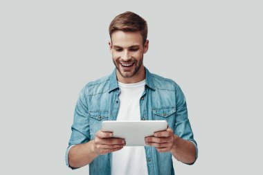 Yakışıklı genç adam gülümseyen ve gri arka plan karşı dururken dijital tablet kullanarak