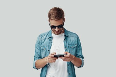 Yakışıklı genç adam gri arka plan karşı dururken müzik dinliyor