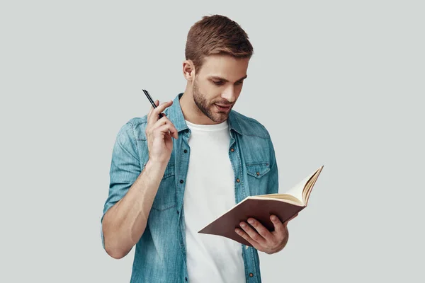 Handsome young man writing something while standing against grey background — Stock Photo, Image