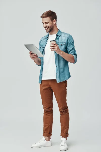 Comprimento total de belo jovem sorrindo e usando tablet digital enquanto está de pé contra fundo cinza — Fotografia de Stock