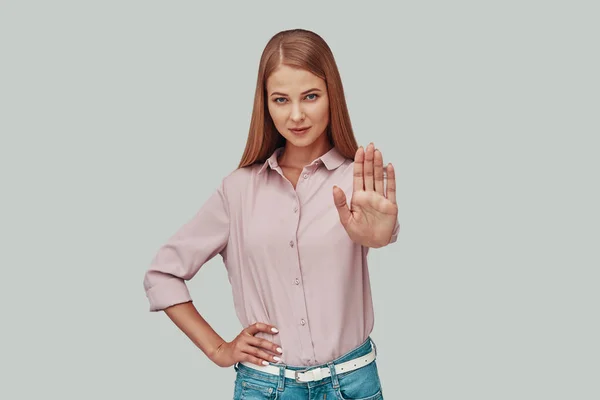 Atractiva mujer joven mostrando gesto de stop mientras está de pie sobre fondo gris —  Fotos de Stock