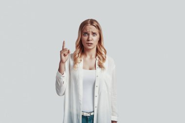 Hüsrana uğramış genç bir kadın kameraya bakıyor ve gri arka planda dururken fotokopi alanını işaret ediyor.