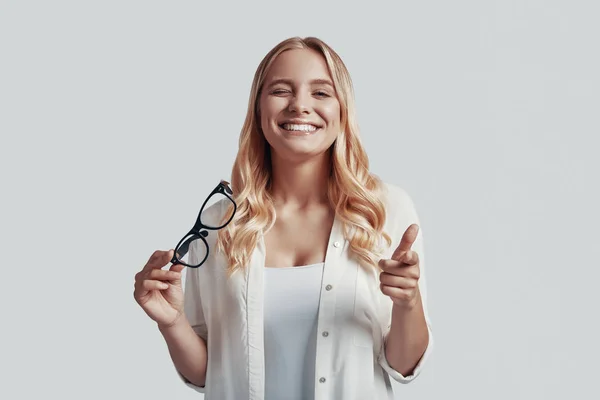 Atractiva joven mujer señalándote y guiñando un ojo con sonrisa mientras está de pie sobre un fondo gris —  Fotos de Stock