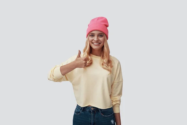 Atractiva joven mujer haciendo gestos y sonriendo mientras está de pie sobre un fondo gris — Foto de Stock