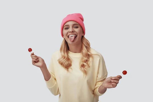 Attractive young woman sticking out tongue and looking at camera while standing against grey background — Stock Photo, Image