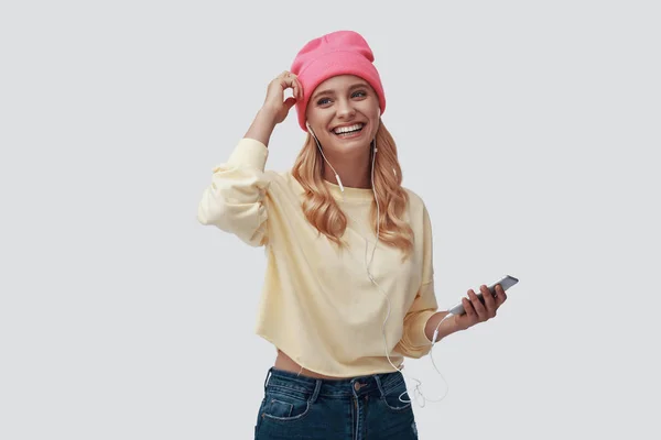 Atractiva joven mujer mirando a la cámara y sonriendo mientras está de pie sobre un fondo gris — Foto de Stock