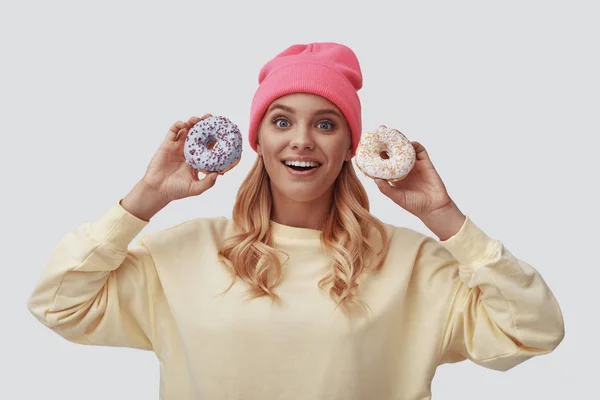 Attractive young woman holding donuts and looking at camera while standing against grey background — Stock Photo, Image