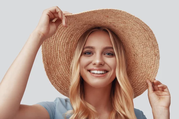 Atraente jovem mulher sorrindo e olhando para a câmera enquanto em pé contra fundo cinza — Fotografia de Stock