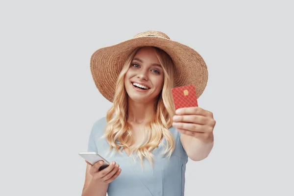 Привлекательная молодая женщина улыбается и показывает кредитную карту, стоя на сером фоне — стоковое фото