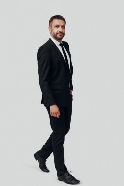 Tam takım elbiseli yakışıklı bir genç, gri arka planda kameraya bakıyor.