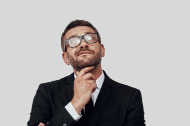 Yakışıklı, takım elbiseli genç bir adam. Gri arka planda dikilirken ellerini çenesinden ayırmıyor.