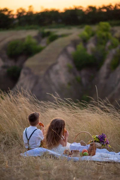 子供の日日没時の子供たちはピクニックに座っています 子供たちは公園で食事をします 自然の中で子供たちはロールを食べます — ストック写真