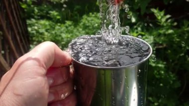 Kristal temiz su el yavaş hareket metal fincan dökülür. Su tasarrufu ve içecek suyu konsepti. Kamp ve hayatta kalma.