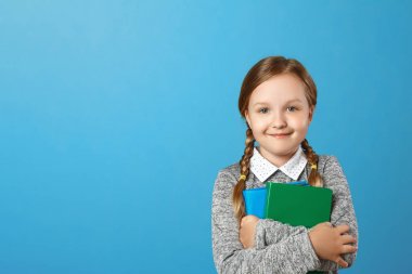 Mavi arka plandaki küçük bir kız öğrencinin yakın çekim portresi. Çocuğun elinde kitap var. Eğitim ve okul kavramı. Kopyalama alanı