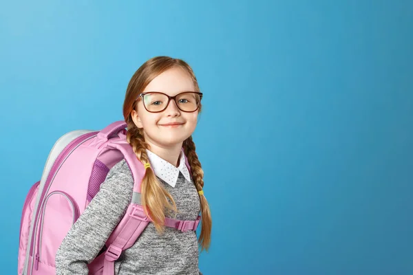 Portret van een klein meisje schoolmeisje met een rugzak op een blauwe achtergrond. Terug naar school. Het begrip onderwijs. Ruimte kopiëren. — Stockfoto