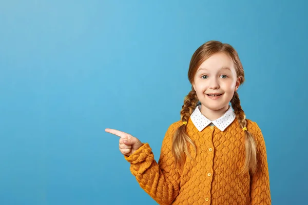 Je to portrét malé dívčí dívky na modrém pozadí. Dítě ukazuje na stranu. Kopírovat místo. — Stock fotografie