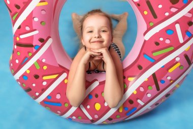 Bir çocuk stüdyoda lastik bir yüzükle oynar. Küçük kız kameraya bakıyor. Mavi arka plan.