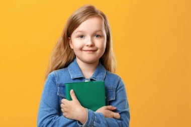 Küçük kız sarı bir arka plan üzerinde kot gömlek li öğrenci. Çocuğun elinde bir kitap var. Eğitim ve okul kavramı.