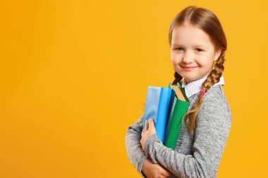 Sarı arka planda at kuyruklu küçük bir kız öğrenci portresi. Çocuğun ders kitapları var. Eğitim ve okul kavramı. Kopyalama alanı.